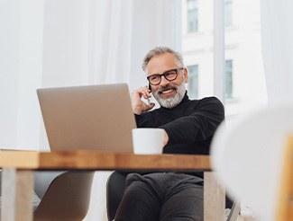 Man with glasses smiling while working on laptop