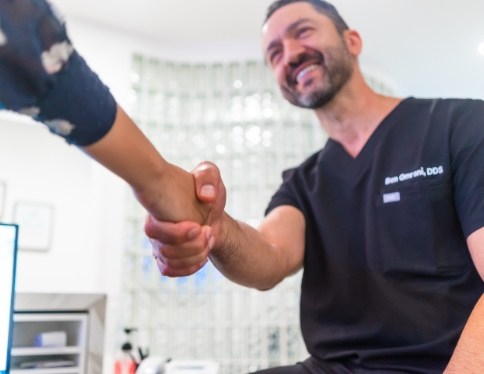 Smiling dentist shaking hands with dental patient