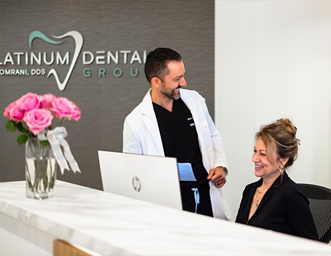 Dentist and dental team member laughing together at reception desk