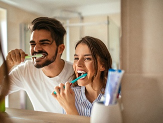 Man and woman smiling while brushing teeth in bathroom