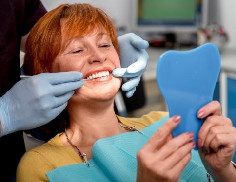 Woman looking at smile enjoying the benefits of dental implants