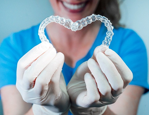 dentist holding two clear aligners in the shape of a heart 