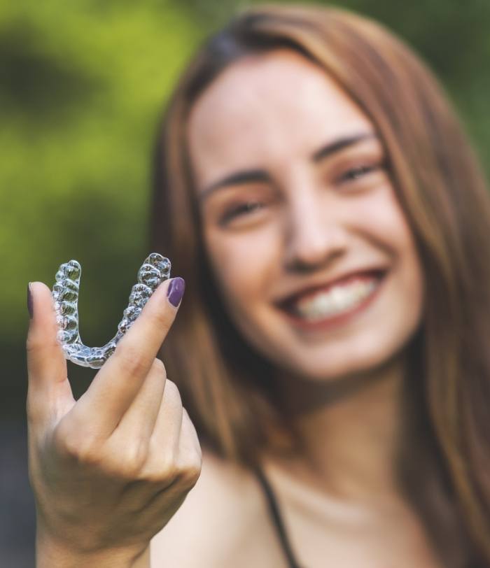 Smiling woman holding up an Invisalign tray