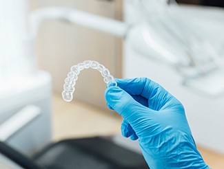 Dentist with blue glove holding clear aligner