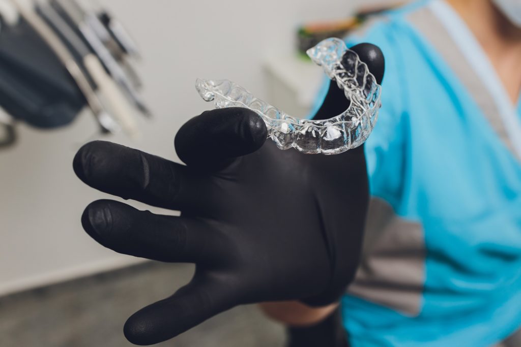 Dentist holding Invisalign aligner with black glove