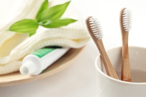 Two toothbrushes in cup sitting next to toothpaste and towel